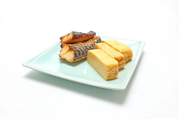 Grilled mackerel with salt and Japanese-style rolled omelette on a dish isolated on a white background.
