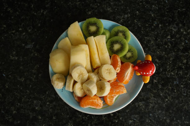 fruit plate, plate with chopped apple, kiwi, banana and tangerine, on dark background