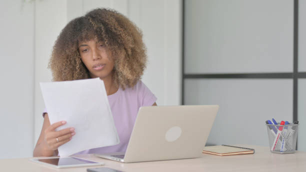 istock Young African Woman Working on Documents and Laptop at Work 1465114019