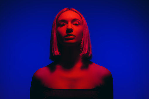 Young female with fair hair looking at camera against blue backdrop in studio with neon illumination