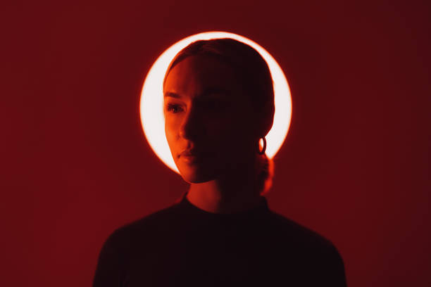 Calm female with earrings looking at camera against shiny light in dark studio with red neon illumination