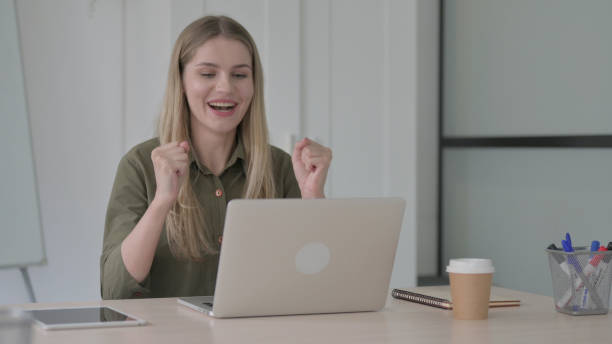 istock Young Blonde Woman Celebrating Success while using Laptop 1465118893
