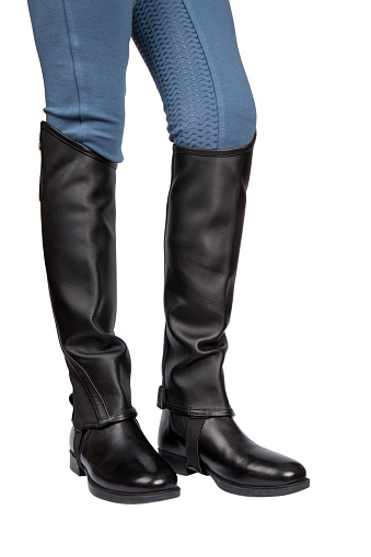 The legs of a woman in black boots, leather mini chap and leggings for horseback riding