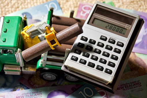 New Zealand Money (NZD), a calculator and a toy logging truck for a concept image for the cost of a running a work vehicle.