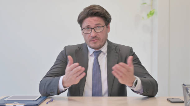 istock Online Video Chat by Talking Middle Aged Businessman in Office 1465131663