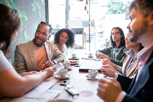 Diverse group of businesspeople talking while working together through their lunch at a table in a cafe