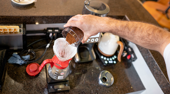 Close-up of a male barista pouring freshly ground coffee grains into a pot at the counter of a cafe