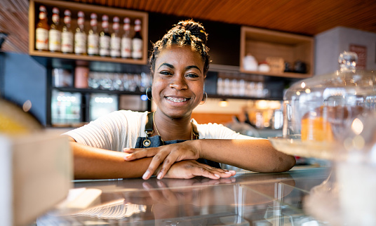Portrait of a young female barista with braces smiling while working behind the counter of a bakery and cafe
