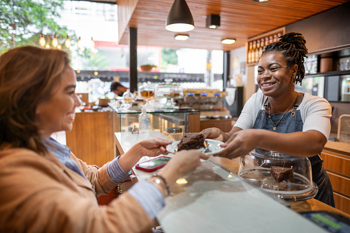 Smiling female barista passing a customer a slice of chocolate cake over a counter at a bakery and cafe