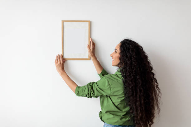 istock Lady Hanging Picture In Frame On Wall Decorating House Indoors 1465136558