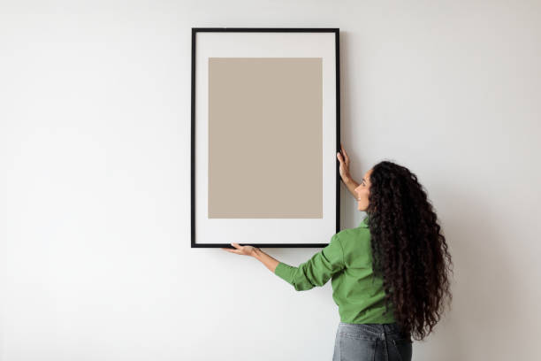 istock Happy Woman Hanging Empty Poster In Frame On Wall Indoors 1465136562
