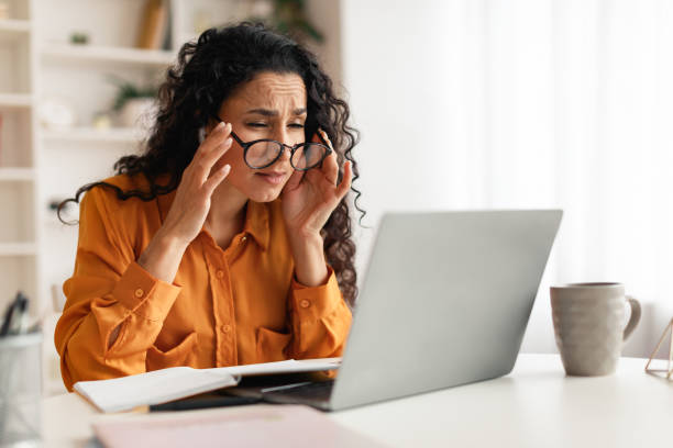 Woman With Poor Eyesight Wearing Eyeglasses Looking At Laptop Indoors Poor Eyesight. Middle Eastern Woman Wearing Eyeglasses And Squinting Eyes Looking At Laptop Screen Sitting At Workplace Indoors. Ophtalmology, Bad Vision Health Problems Concept squint eyes stock pictures, royalty-free photos & images