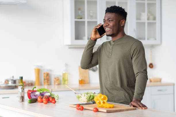 istock Phone Call. Handsome Young Black Guy Talking On Cellphone In Kitchen Interior 1465137216