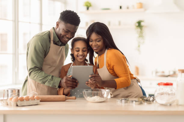 Black Family Baking Using Digital Tablet Cooking Cake In Kitchen