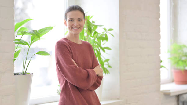 istock Smiling Beautiful Woman Smiling Looking at Camera while Standing Near Window 1465139538