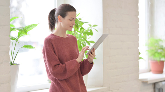 Young Woman Using Tablet while Standing Near Window