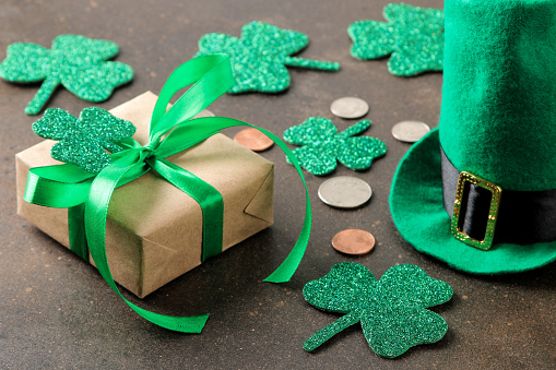 St.Patrick 's Day. celebration. Green leprechaun hat, money and clover leaf and gift box on brown background.