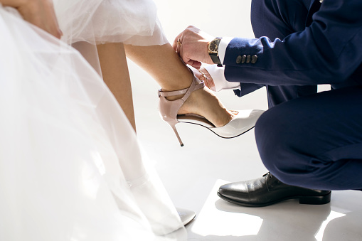 polite man helps a woman to put on her shoes. The groom takes care of his bride and on the wedding day neatly buttons up women's high-heeled shoes. Female shoes and male hands close up