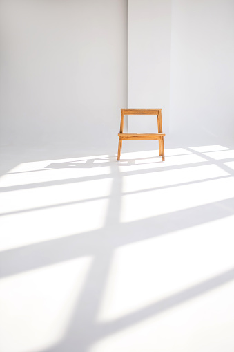 Wooden chair in a white room with shadows from the windows. Stylish minimalism in the form of a single chair in a clean white room. Shadows on the floor from the windows near the chair