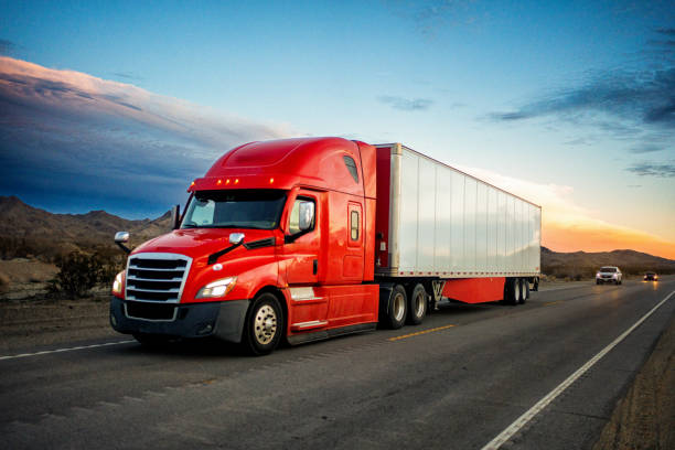 semi-remorque de couleur rouge vif roulant à toute vitesse sur une autoroute à deux voies avec des voitures en arrière-plan sous un magnifique coucher de soleil dans le sud-ouest américain - semi truck truck highway red photos et images de collection