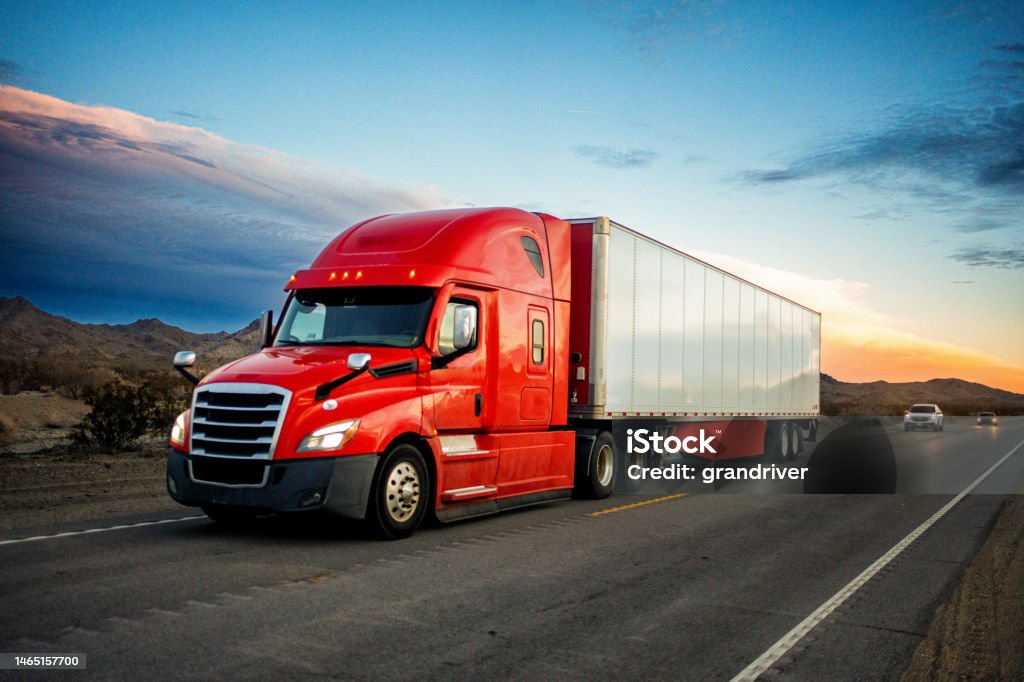 Brightly Red Colored Semi-Truck Speeding on a Two-Lane Highway with Cars in Background Under a Stunning Sunset in the American Southwest Truck Stock Photo