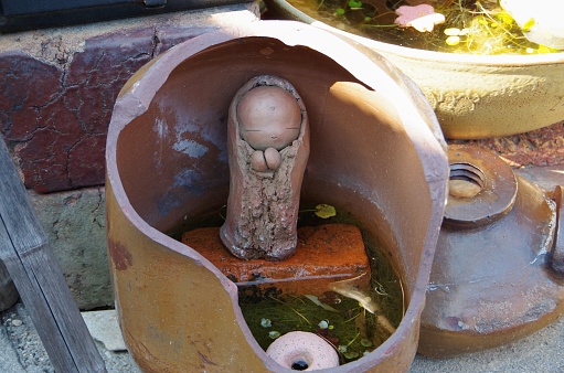 Idyllic view of an old rusty bird bath with water in a beautiful green and growing summer garden with flowering plants. Seen in Germany in June.