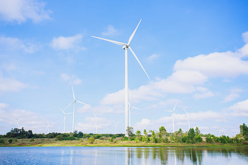 Powerful Wind turbine farm for pure energy production on Beautiful clear blue sky with white clouds and wind turbine farm reflection on lake. renewable energy