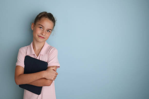 分離型青の背景にピンクのシャツを着た小さな感情的な10代の女の子11、12歳、手にタブレットを持つ。子供のスタジオのポートレート。碑文の場所をコピーするテキストを配置します - 10 11 years child human face female ストックフォトと画像