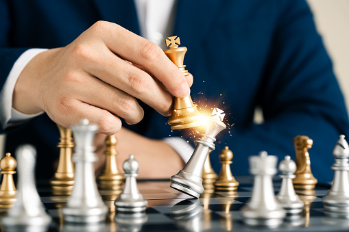 leadership concept, businessman hand catches golden chess king checkmate in chessboard tournament, business team challenge, winner in global industry.
