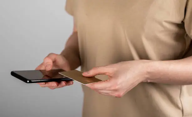 Close up hands holding credit card and smartphone, paying online, using banking service, mobile phone app, entering information, bankcard data, shopping, ordering in internet store. High quality photo