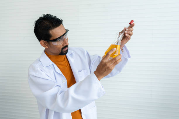Male teacher in white lab coat with safety glasses preparing lab tools for teaching students in university science classroom.