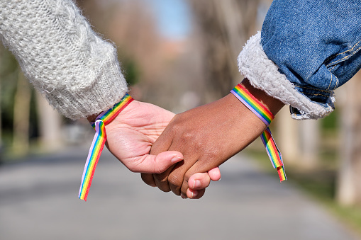 hands of interracial lesbian couple with lgbt rainbow bracelets