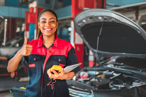 Auto service, repair, maintenance concept. Mechanic checks the car at the service station.African american woman  engineer use tablet check car battery .