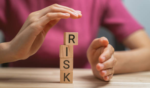 istock Hand preventing falling wooden blocks with risk word. 1465218730
