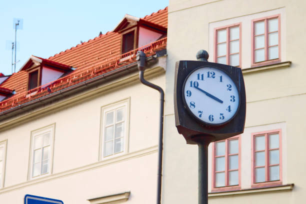 Old street clock in Prague against the house with beautiful windows.