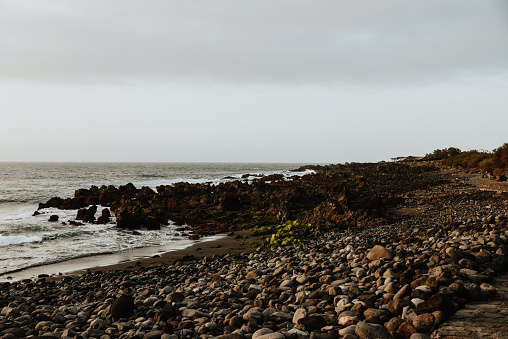 A landscape of a beach covered in pebbles surrounded by the sea under a cloudy sky