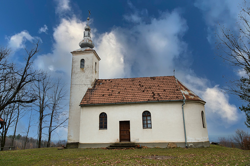 A beautiful white church with a rusty roof surrounded by dry trees under a cloudy sky