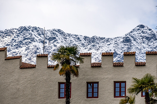 The facade of a building with a battlement wall against a snowy rock mountain