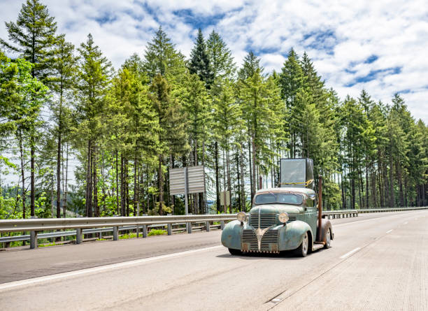 Retro old style rusty small truck tractor with small dump trailer transporting fastened cargo driving on the wide highway road as a professional owner operator big rig