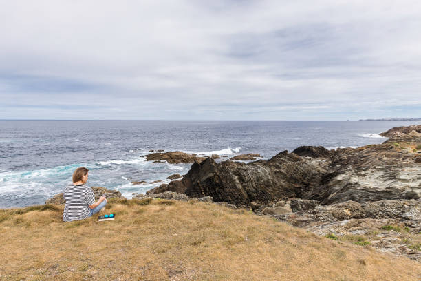istock woman sitting on grass using her phone by the sea 1465237613