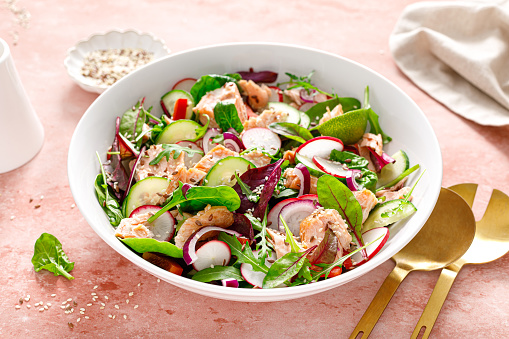 Salmon salad bowl with fresh radish, cucumber, red onion and green mixed leafy vegetables. Healthy diet food, lunch menu