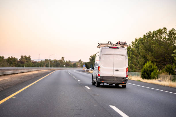 Small cargo mini van with ladder on the roof driving on the road to point of the service stock photo