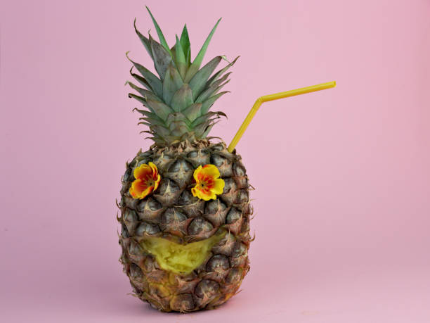 istock Pineapple with a plastic straw, flower eyes, and a carved smile on a pink background 1465242908