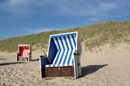 Several beach chairs on a sandy beach under a blue cloudy sky in Sylt, Germany