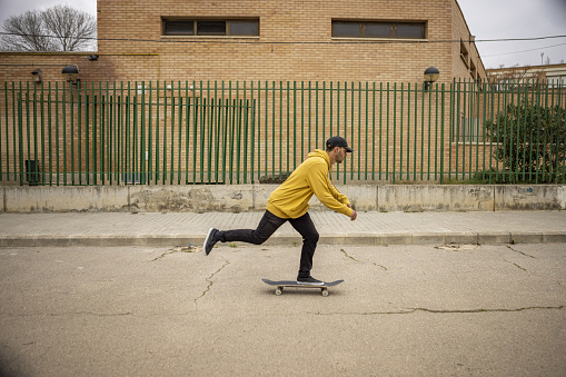 A young caucasian male from Italy skateboarding on the street in a yellow hoodie and a black cap