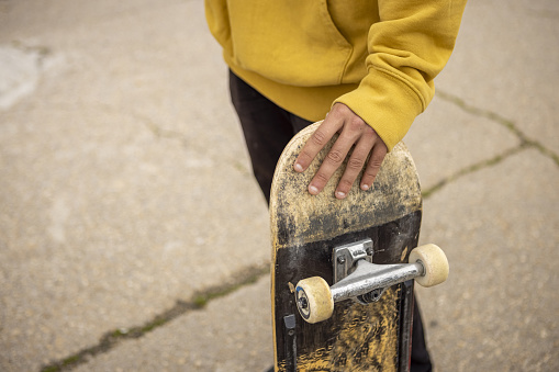 A high angle shot of a hand holding a skateboard on the street