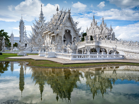 Wat Rong Khun in Chiang Rai Thailand. Famous buddhist White Temple in Chiang Rai under summer skyscape with fluffy clouds. White Tempel mirroring in the surrounding pool. Hasselblad X2D 102 MPixel. White Temple - Wat Rong Khun - Chiang Rai, Chiang Mai, Northern Thailand, Southeast Asia