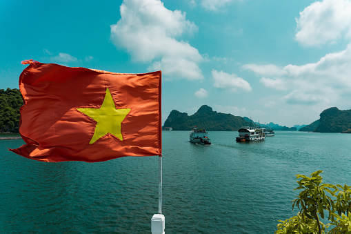 A closeup shot of the National flag of Vietnam on a pole against  sea and ships