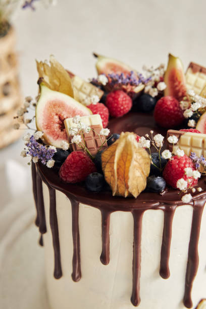 istock Delicious Boho Drip Cake with fruits and flowers on top on a white table 1465251693