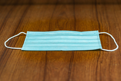A selective focus shot of a blue surgical cotton mask on a wooden surface